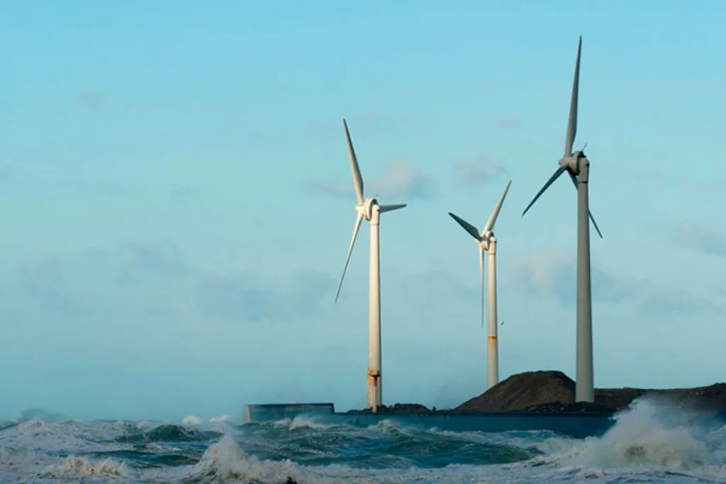 Drei Windturbinen an einem Küstenstreifen mit Wellen, die gegen die Küste schlagen