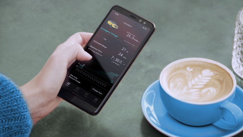 Eine Hand, die ein Telefon hält, das die e:PROGRESS-App auf dem Bildschirm zeigt, mit einem Kaffee im Hintergrund
